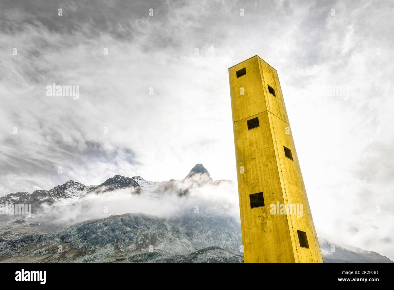 Yellow Origen Tower looms in the sky with mountains in the background. Julier Pass, Graubünden, Switzerland, Europe Stock Photo