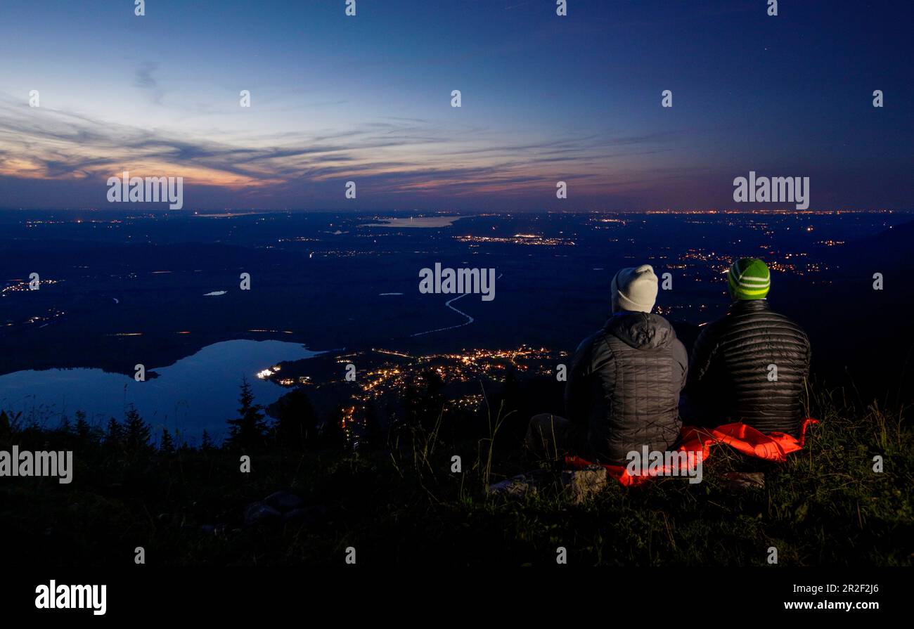 Hikers sit on Jochberg overlooking Kochelsee from above after sunset, Bavaria Stock Photo