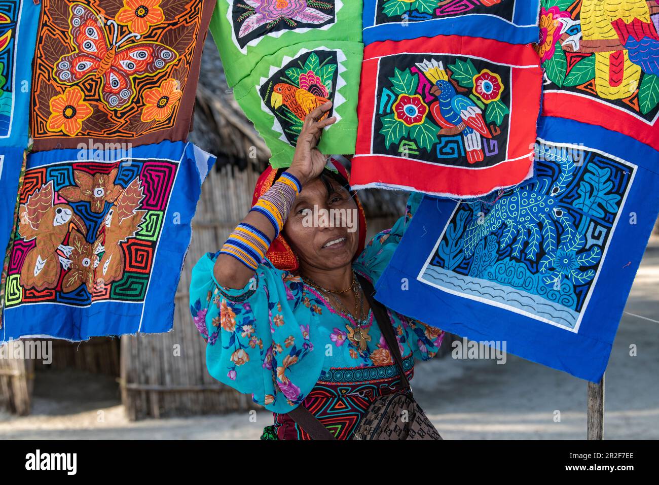 A Guna (formerly Kuna) native woman stands in front of colorful handmade Molas textiles that she sells to tourists, Isla Aroma, San Blas Islands, Pana Stock Photo