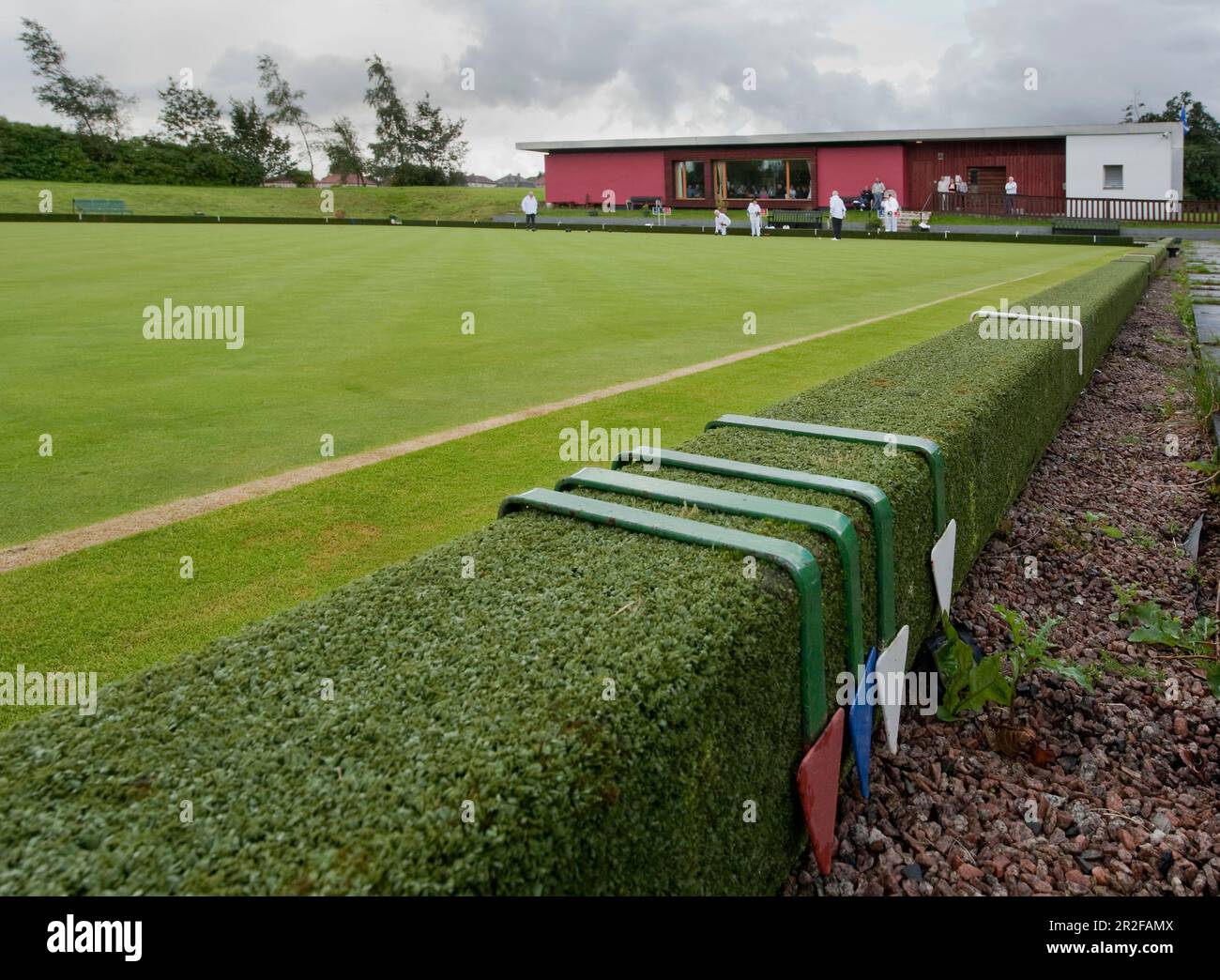Bowls in play in front of flags at the red pavilion clubhouse at the Balornock lawn bowling green in Glasgow, Scotland, UK Stock Photo