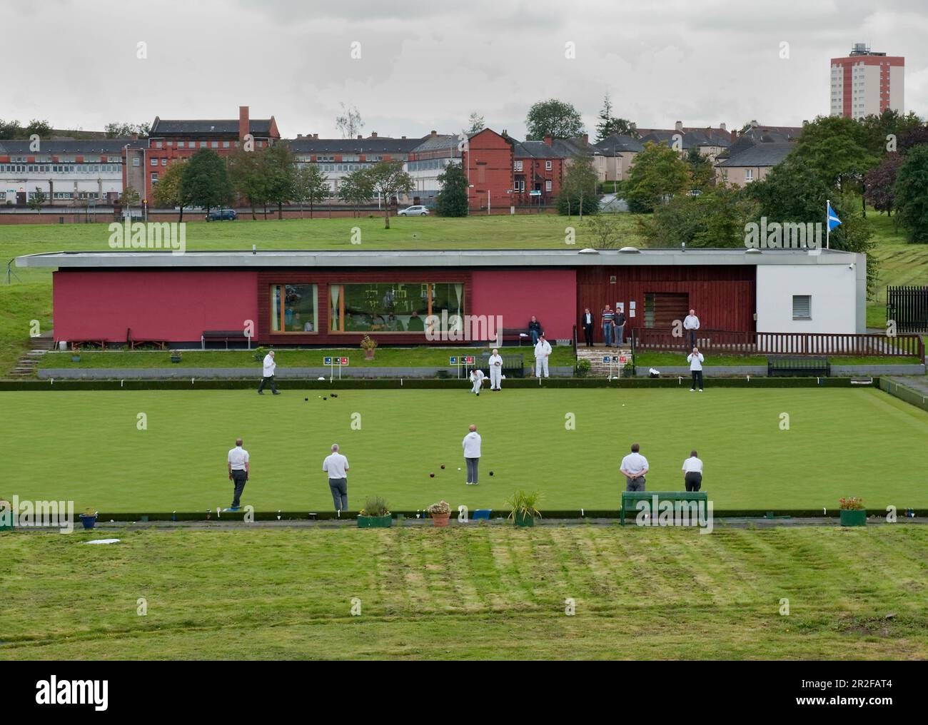Bowls in play within the urban enivornment in front of the red pavilion clubhouse at the Balornock lawn bowling green in Glasgow, Scotland, UK Stock Photo
