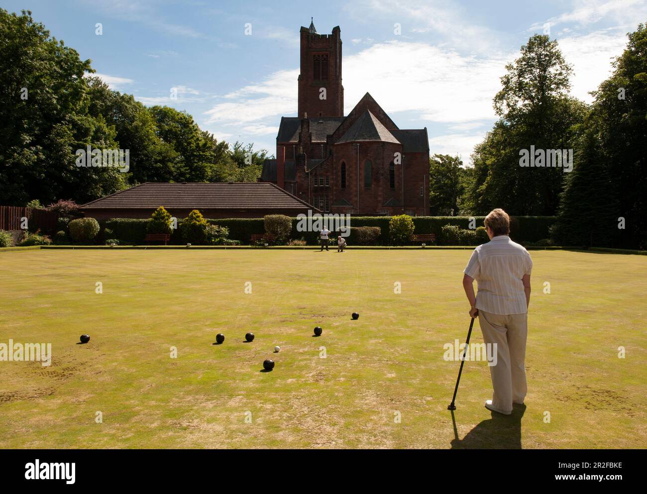 A woman with a walking stick plays bowls at the Kilmarnock lawn bowling green in Kilmarnock, Ayrshire, Scotland, UK Stock Photo