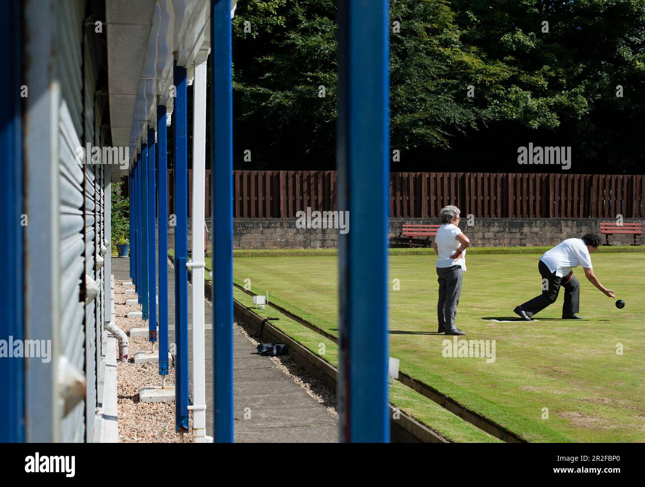 Two women play bowls beside the blue and white metal columns of the pavilion at the Kilmarnock lawn bowling green in Kilmarnock, Ayrshire, Scotland UK Stock Photo