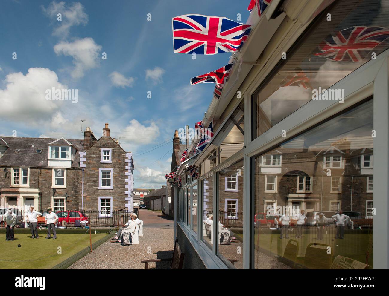 Bowls in play is reflected in the pavilion windows below union jack bunting at the Kirkcudbright lawn bowling green in Dumfries and Galloway, Scotland Stock Photo