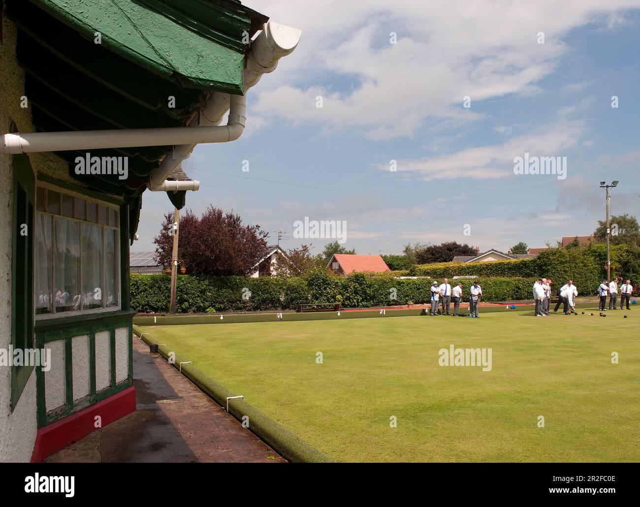 A large crowd of men play bowls in front of the pavilion at the