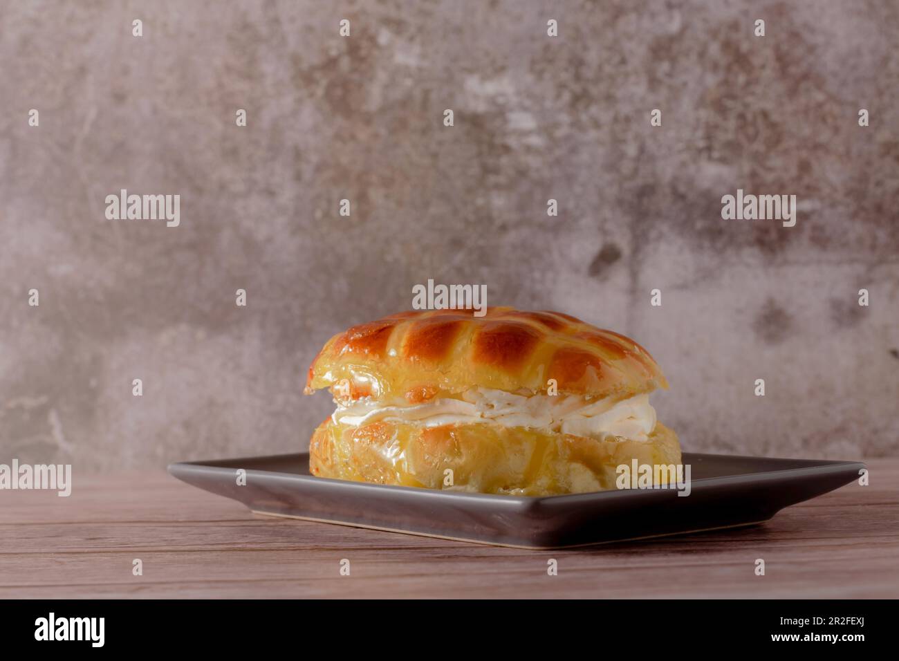 Sweet glazed bun filled with cream on a brown dish on a wooden table Stock Photo