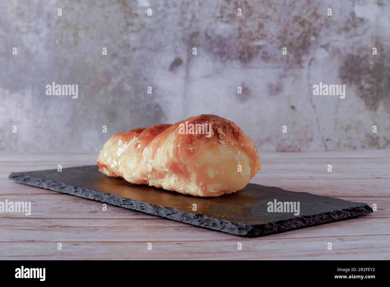 Puff pastry horn filled with pastry cream on a black blackboard on a wooden table Stock Photo