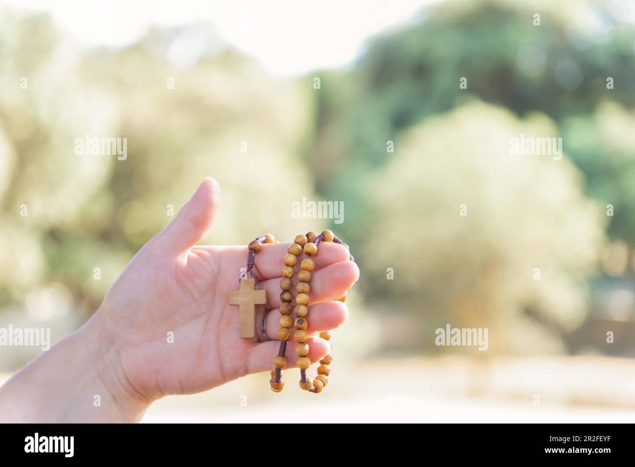 Woman's hands holding a Christian rosary with a cross, praying in a field at dusk Stock Photo