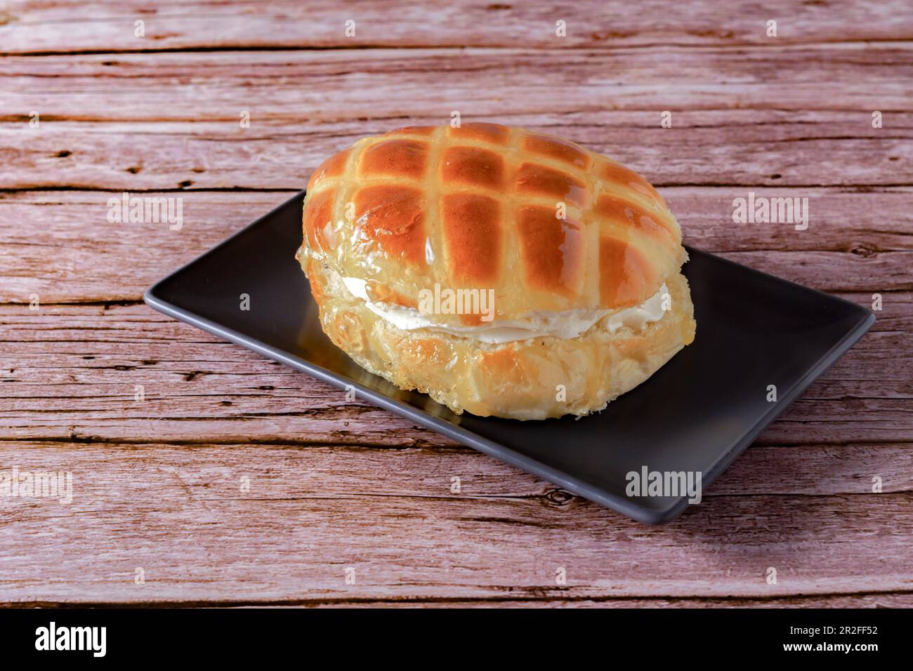 Sweet glazed bun filled with cream on a brown dish on a wooden table Stock Photo