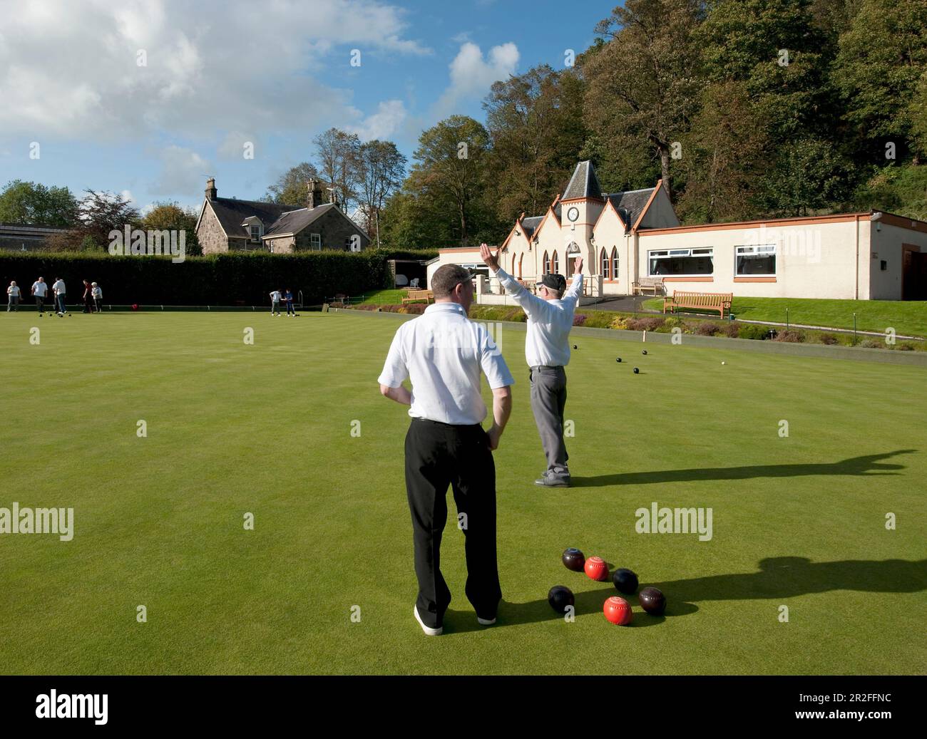 A man raises his arms in victory during Bowls in play in front of the pavilion of the Stirling lawn bowling club green in Stirling, Scotland, UK Stock Photo
