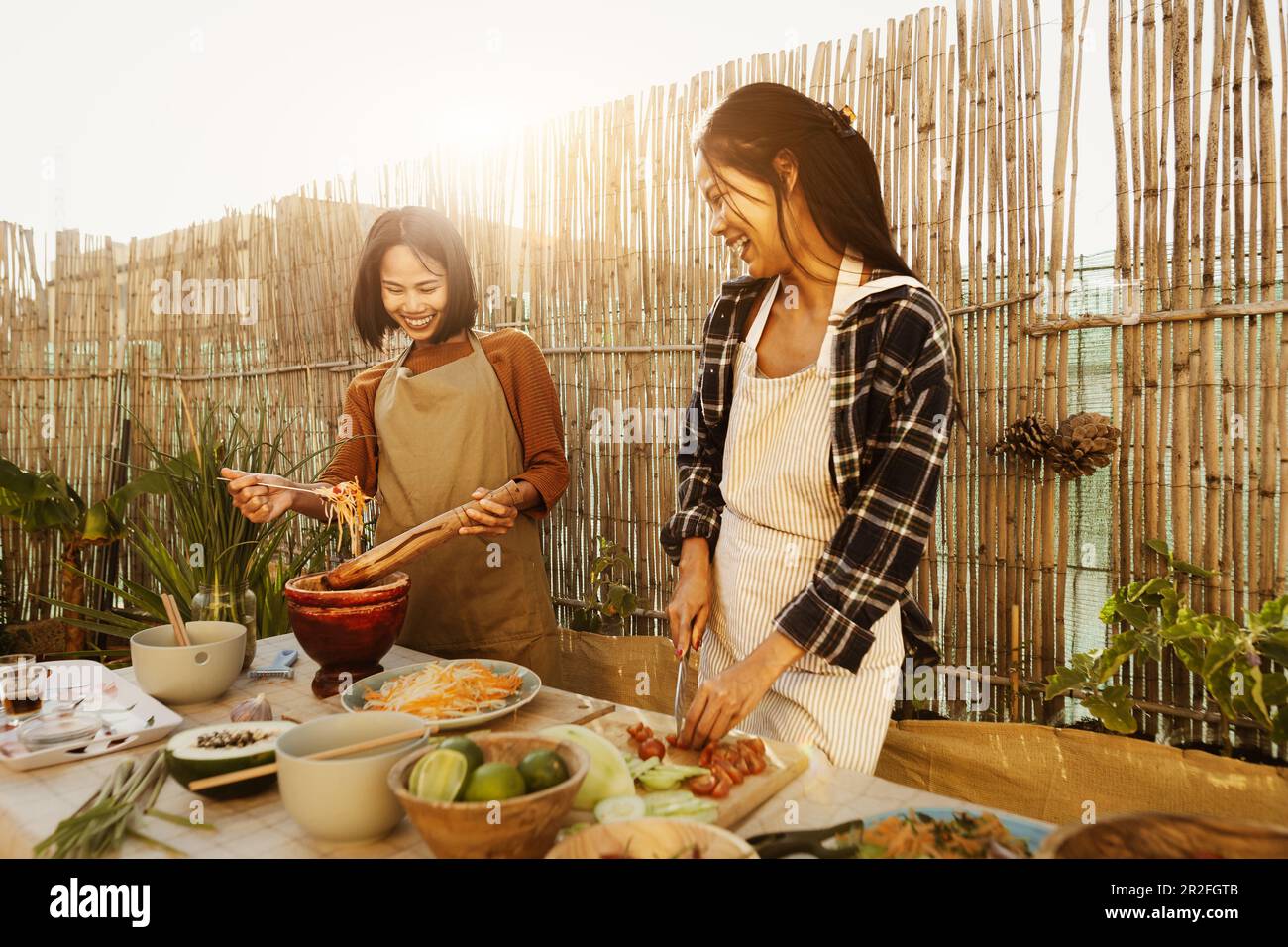 Happy Southeast Asian sisters having fun preparing Thai food recipe together at house patio Stock Photo