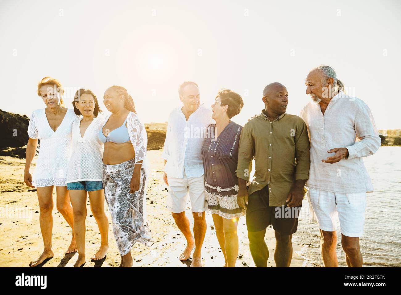 Happy multiracial senior friends having fun walking on the beach during