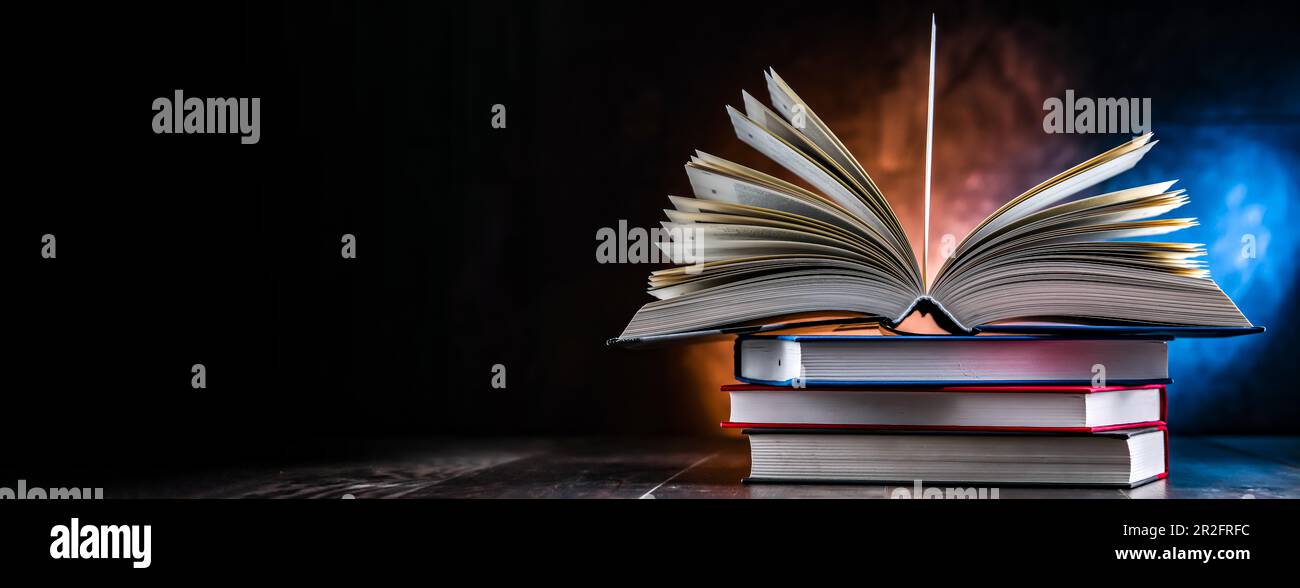 A composition with an open book lying on a stack of other books Stock Photo