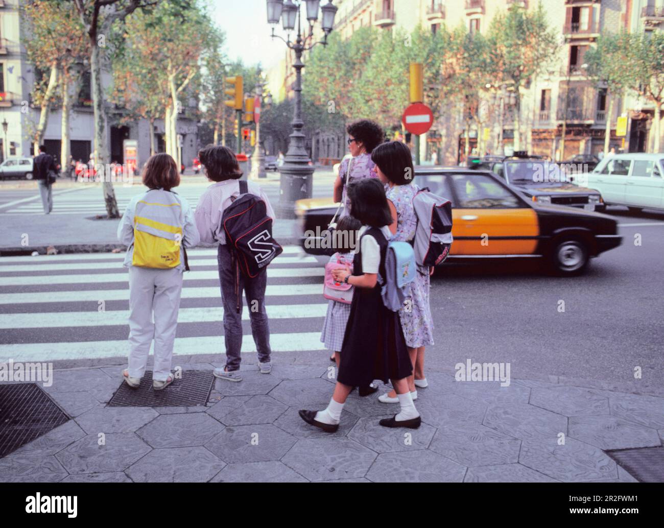 Barcelona Spain Schoolchildren with backpacks. Schoolgirls heading to school. Children in Barcelona at a zebra crossing on street corner. Stock Photo