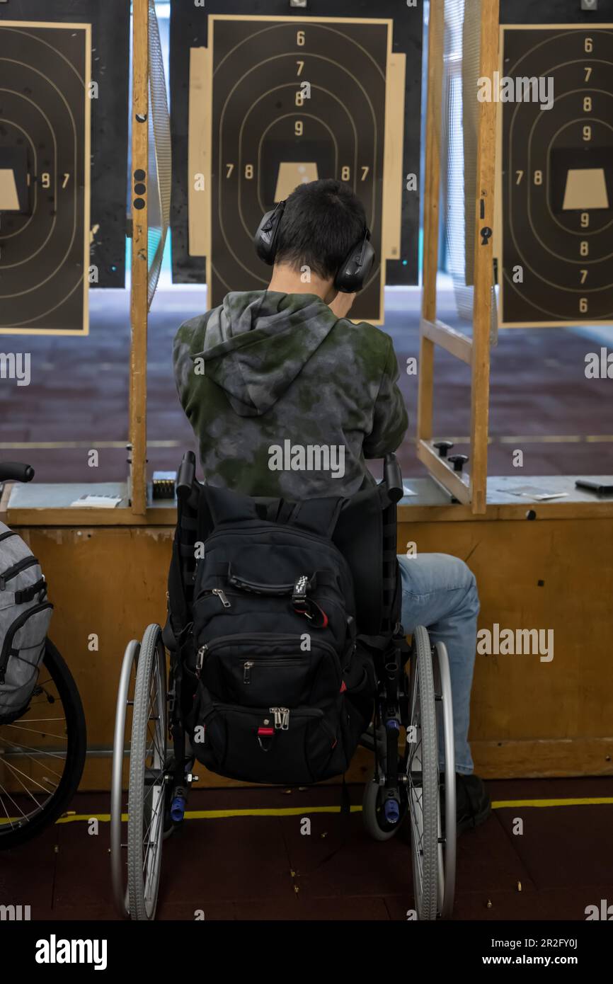 Man in Wheelchair Shooting with a Gun on Shooting Range with Target in