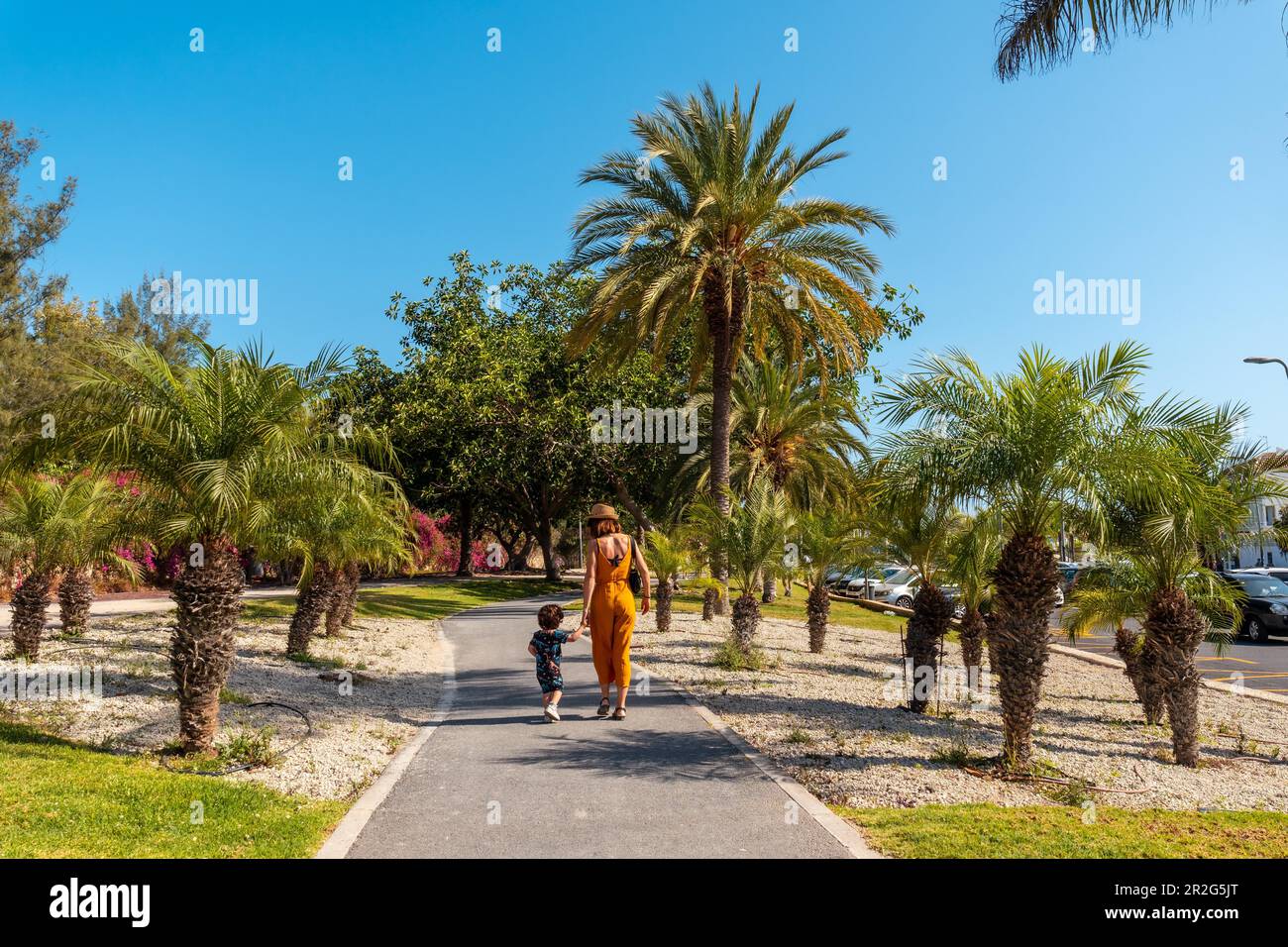 A mother with her son walking through Los Cristianos through a park with palm trees on the island of Tenerife in summer, Canary Islands Stock Photo