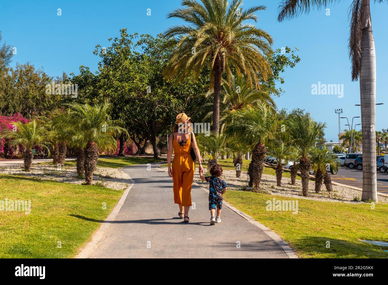 A mother with her son walking through Los Cristianos through a park with palm trees on the island of Tenerife, Canary Islands Stock Photo