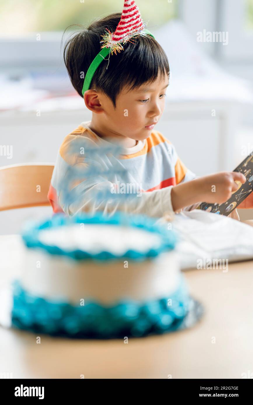 A boy celebrates his birthday. He reads his birthday card before eating the cake. Stock Photo