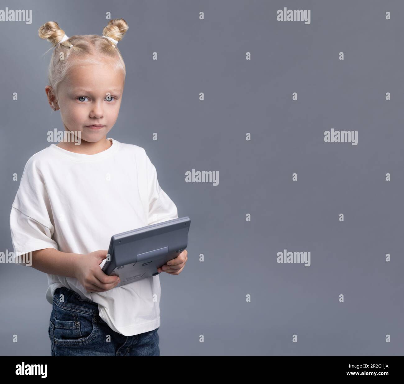 Child with messy buns in white T-short looking at camera on grey background. Little girl holding calculator Stock Photo