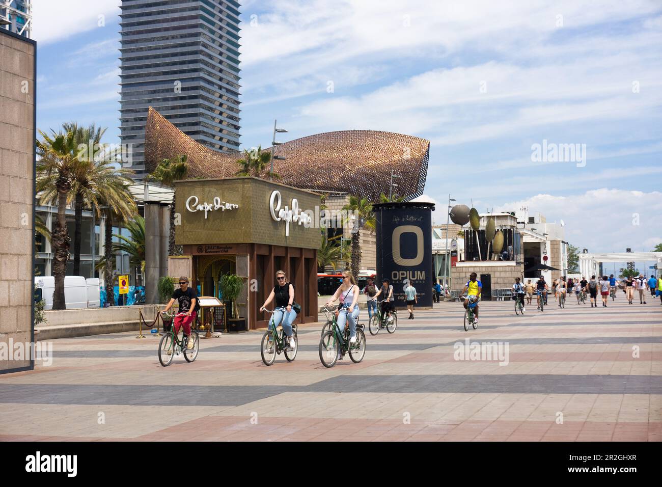 Wide pedestrian thoroughfare with cyclists along the beach in Barcelona, Spain near Olympic village.  Gehery's gold fish pavilion in background. Stock Photo