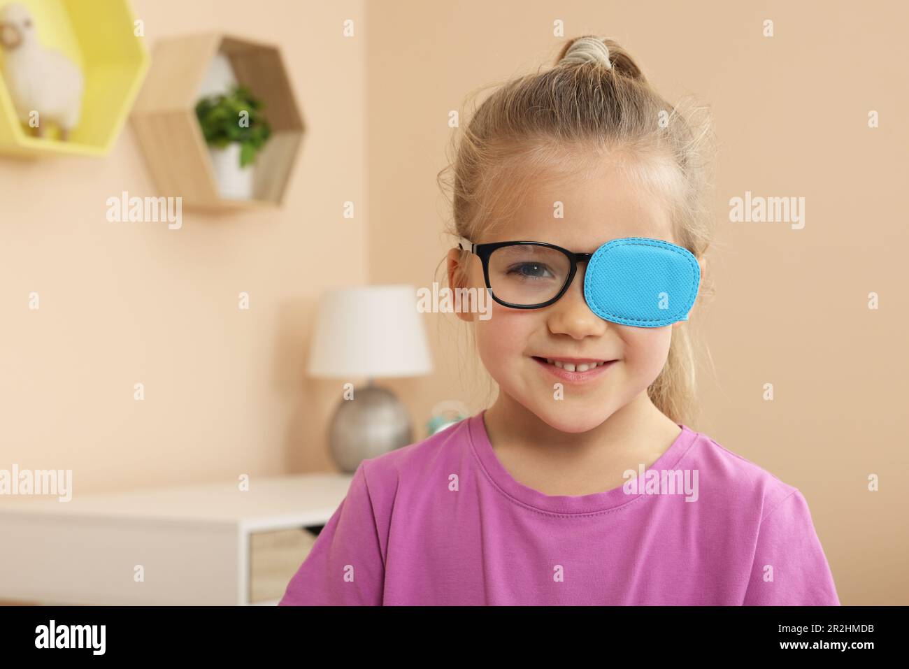 Girl with eye patch on glasses in room, space for text. Strabismus