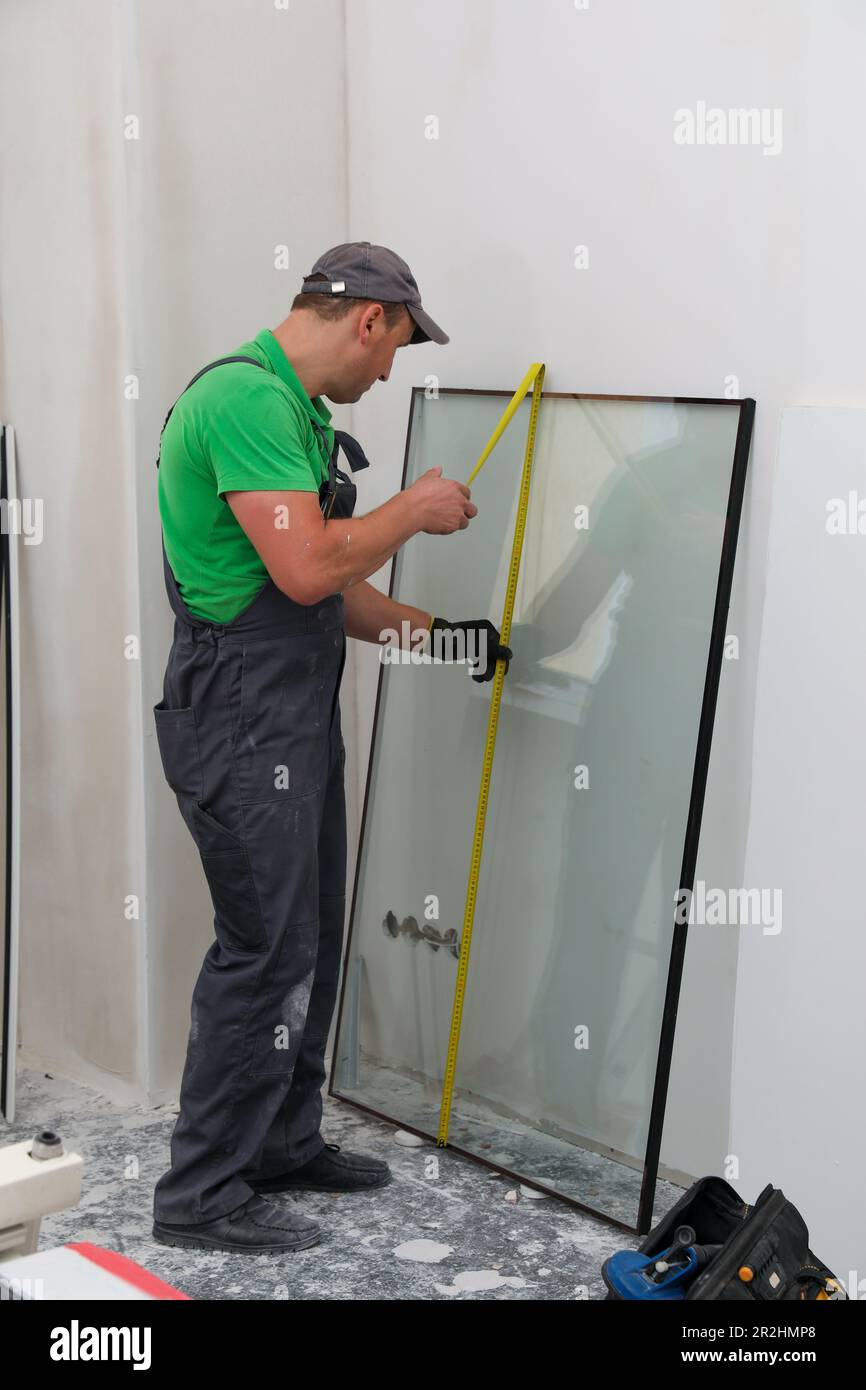 Worker in uniform measuring double glazing window indoors Stock Photo