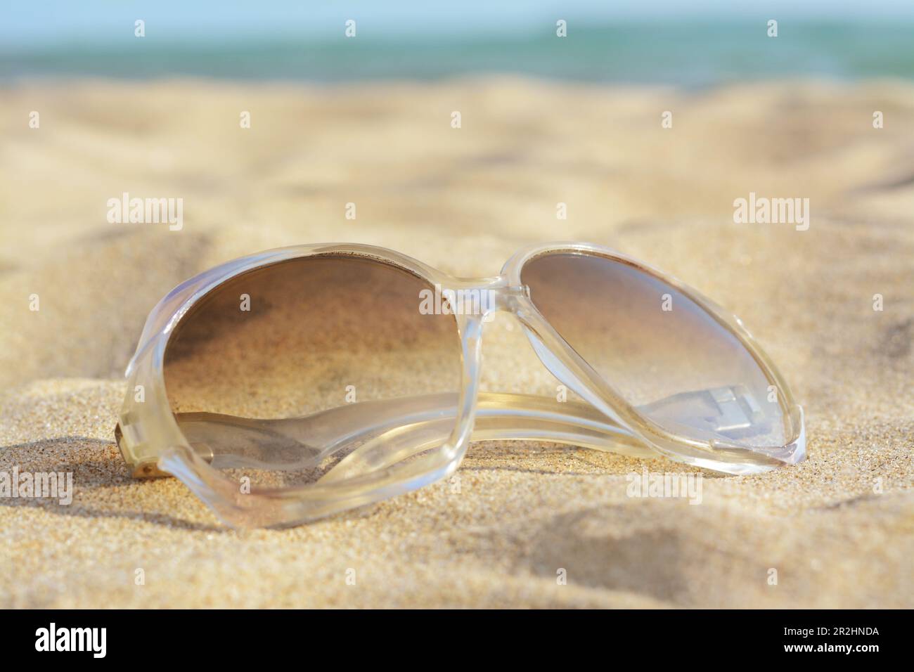 Stylish sunglasses on sandy beach near sea, closeup Stock Photo