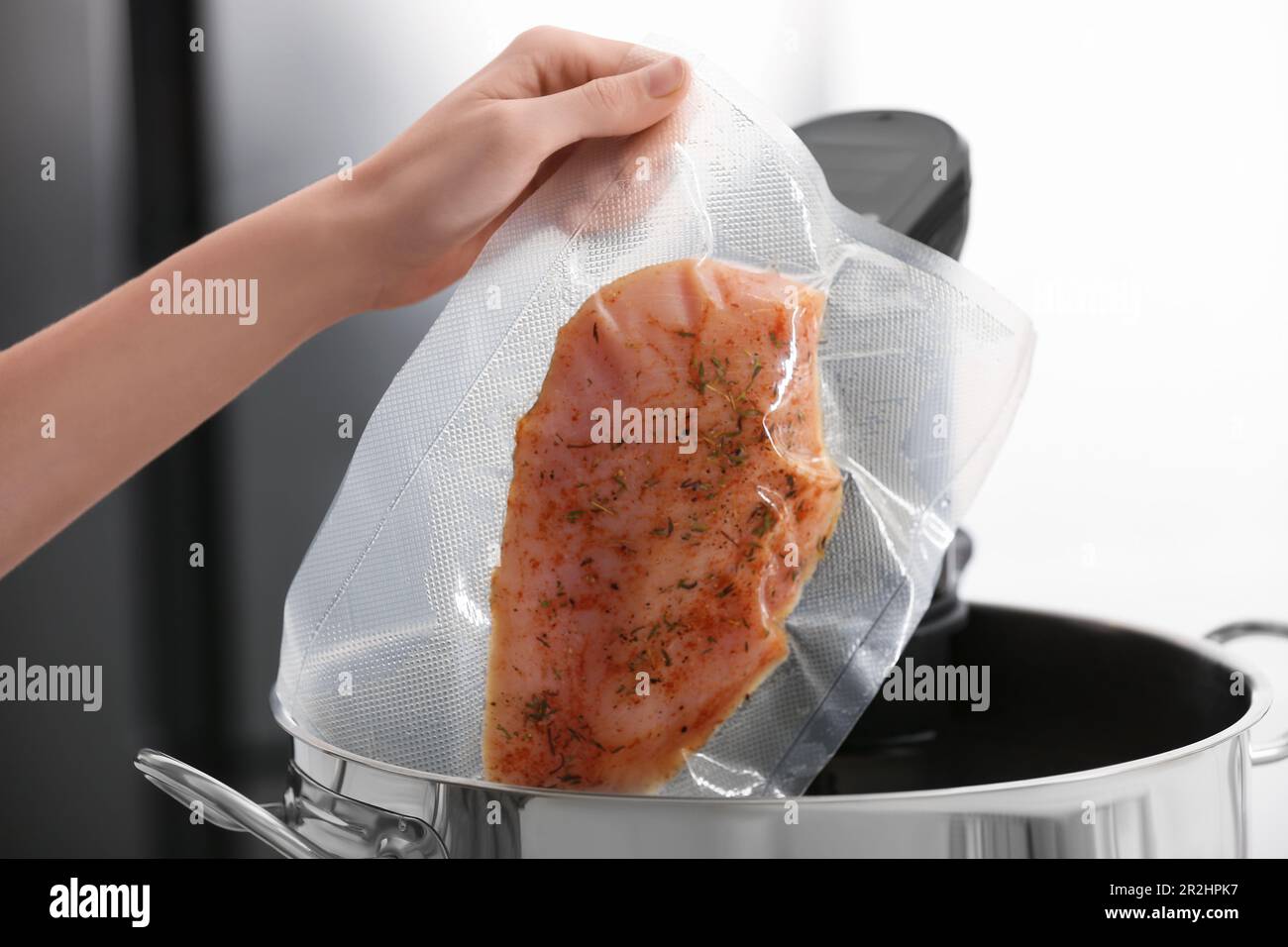 Woman putting vacuum packed meat into pot with sous vide cooker