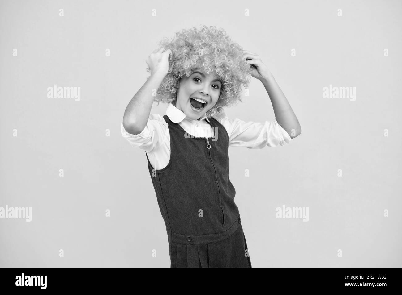 Teenage girl with yellow wig. Funny child wearing orange curly wig hair. Excited face, cheerful emotions of teenager girl. Stock Photo