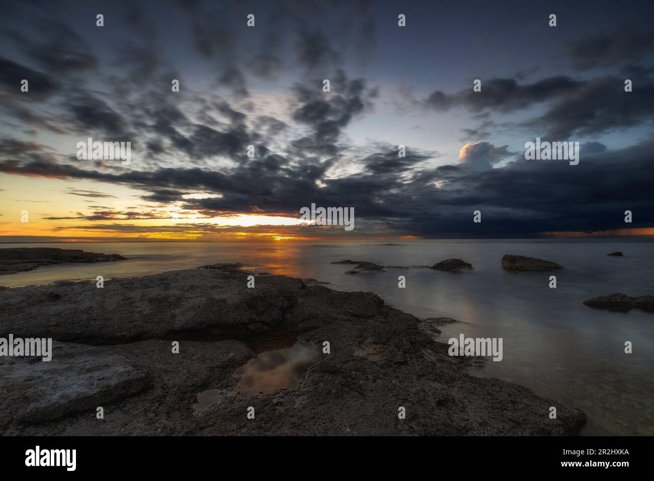 sunset at the sea. Rocky. rain cloud in the background. afterglow. Sky reflects in the water. Lauterhorn, Gotland, Sweden. Stock Photo