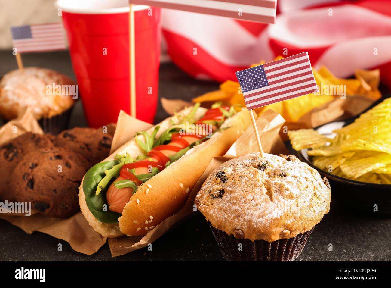 Tasty hot dog, cookies, muffins and snacks for Memorial Day celebration on dark table, closeup Stock Photo