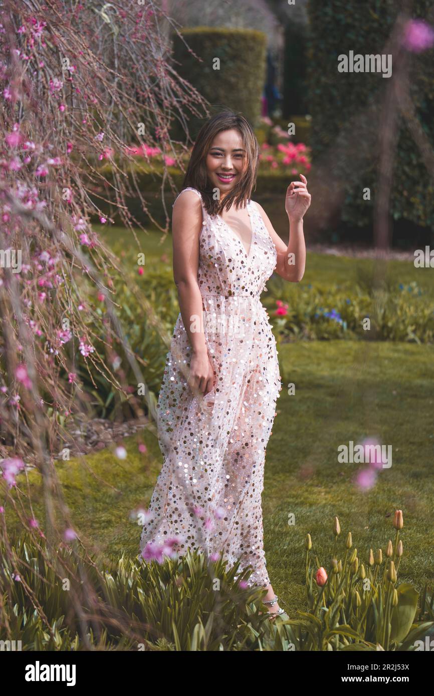 Beautiful Young Woman in Pink Gown Standing Under Blooming Weeping Higan Cherry Tree | Garden | Late Afternoon Stock Photo