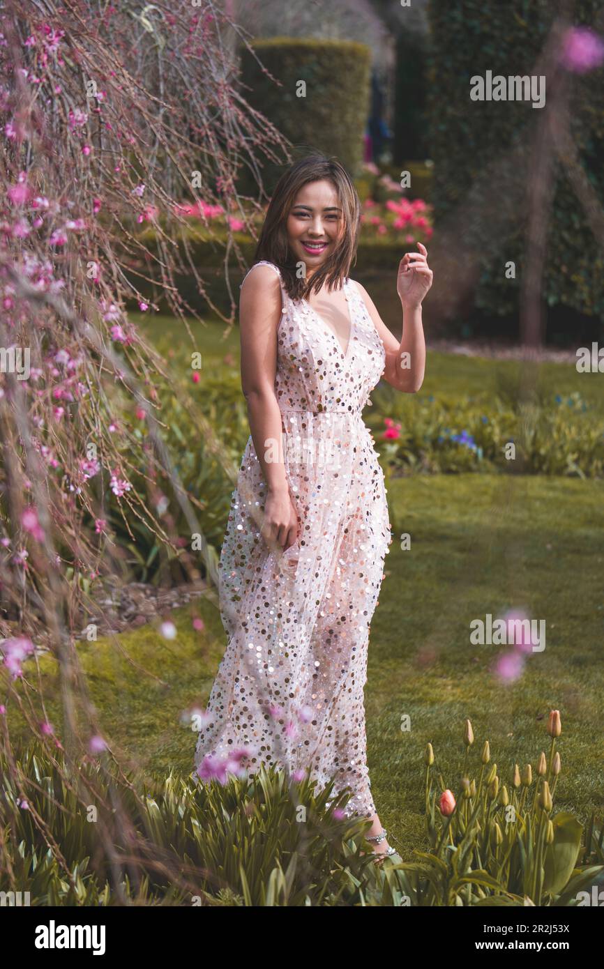 Beautiful Young Woman in Pink Gown Standing Under Blooming Weeping