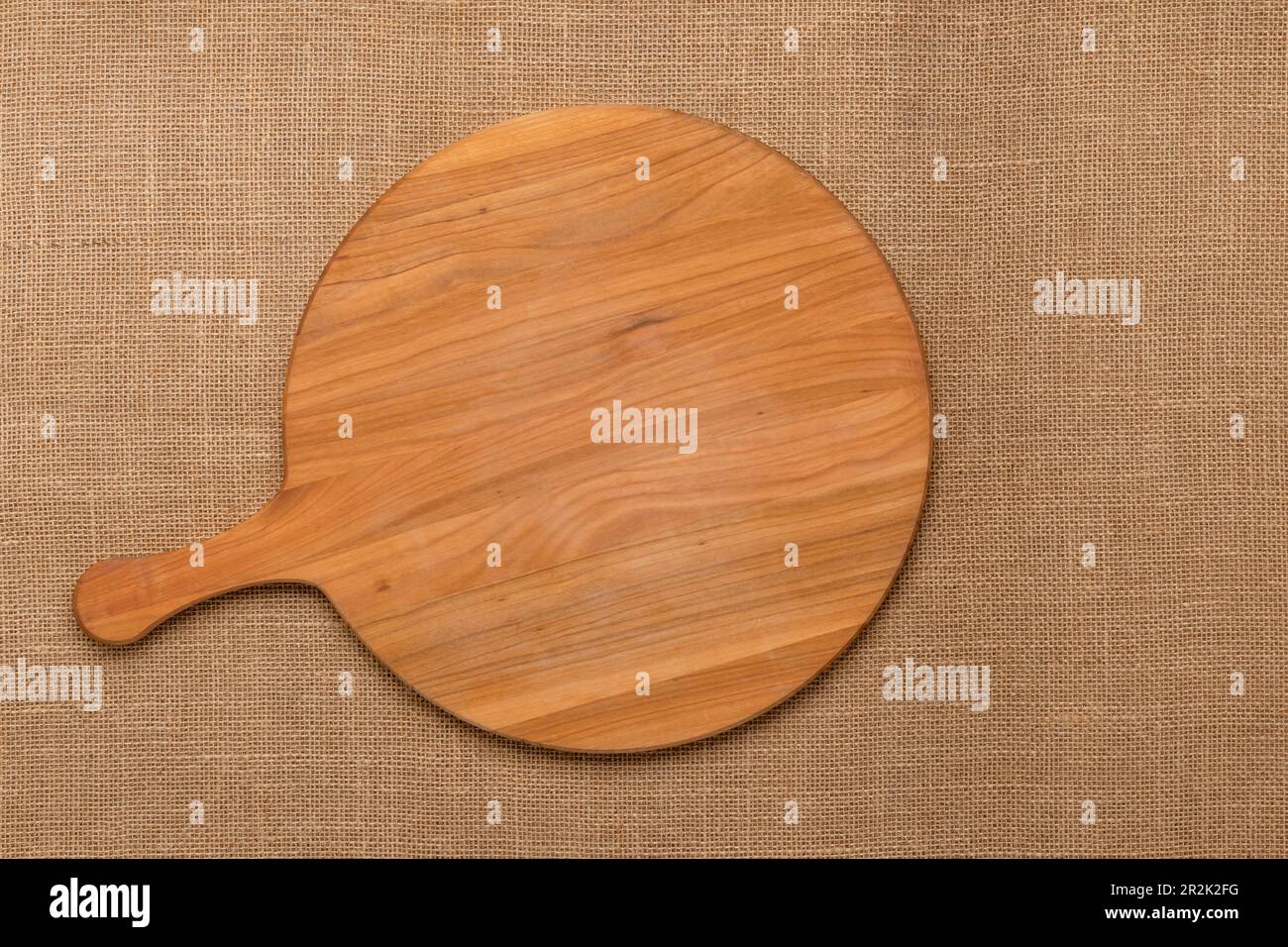 Round empty wooden charcuterie serving board with handle on jute tablecloth. View from above. Minimalist flat design. Cutting board with copy space. T Stock Photo