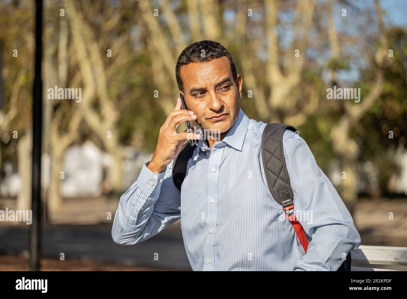 Young latin man sitting on a square bench talking on mobile phone. Stock Photo