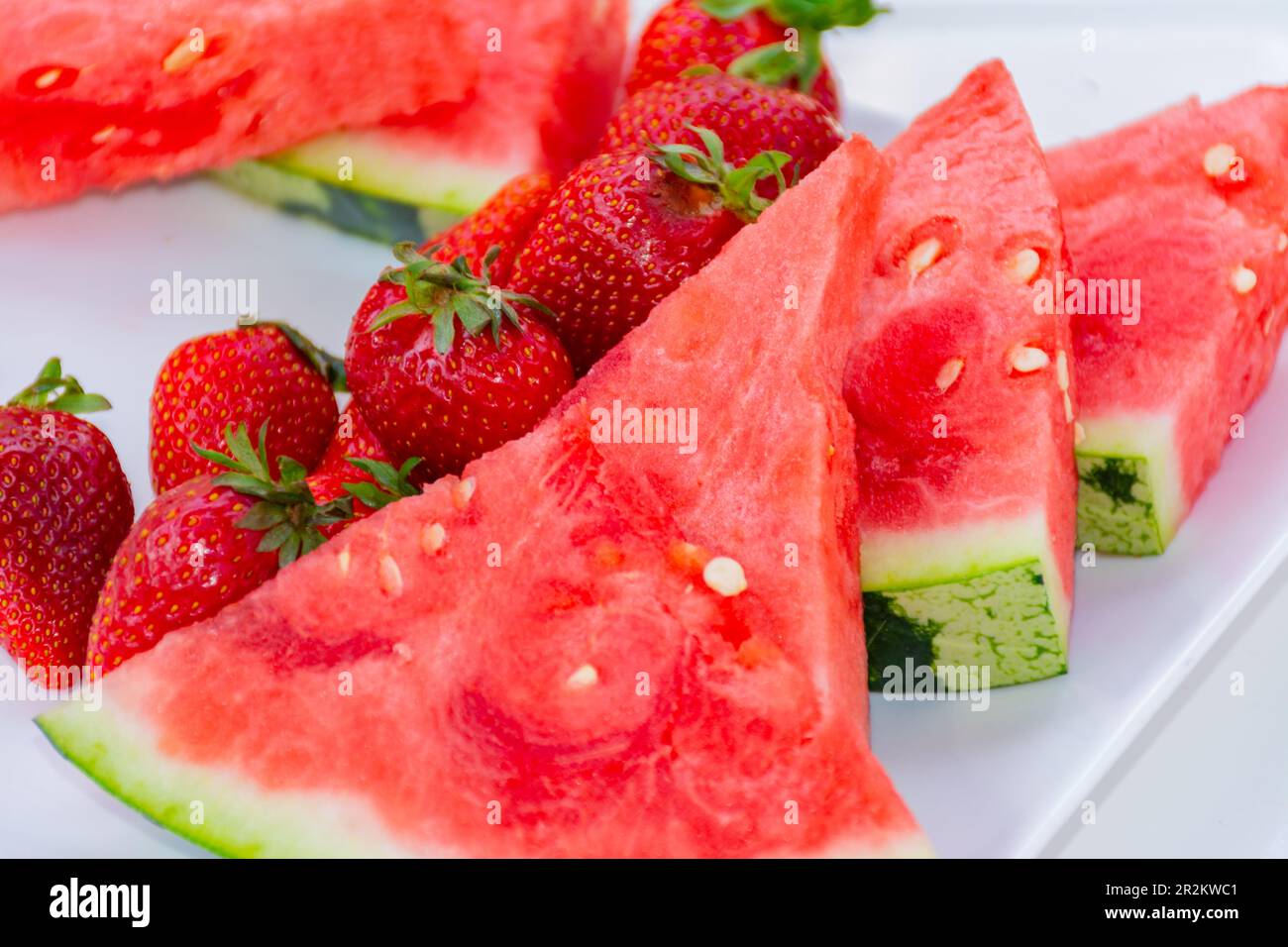 Watermelon slices along with several strawberries on a plate. Summer fruit, fresh and tasty Stock Photo