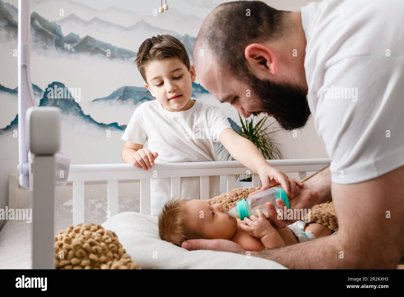 Father and big older brother feed newborn infant with formula