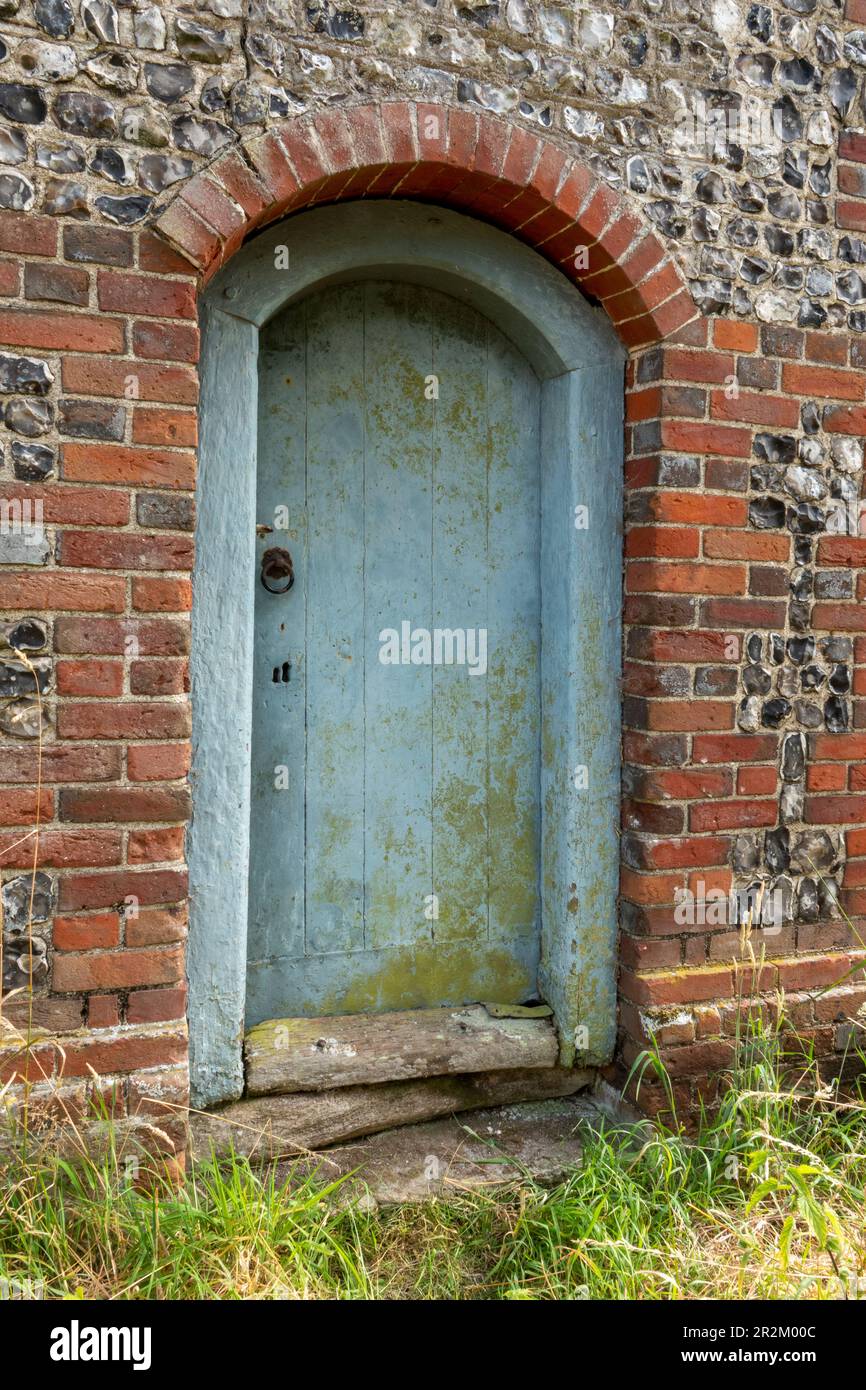 Painted wooden doorway in an old knapped flint and brick building Stock Photo