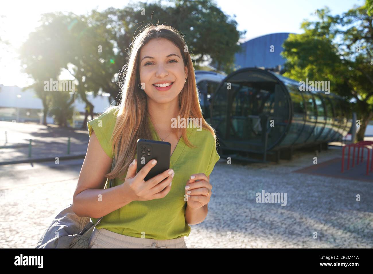 Portrait of happy smiling young woman looking at camera holding phone in Curitiba, Brazil Stock Photo