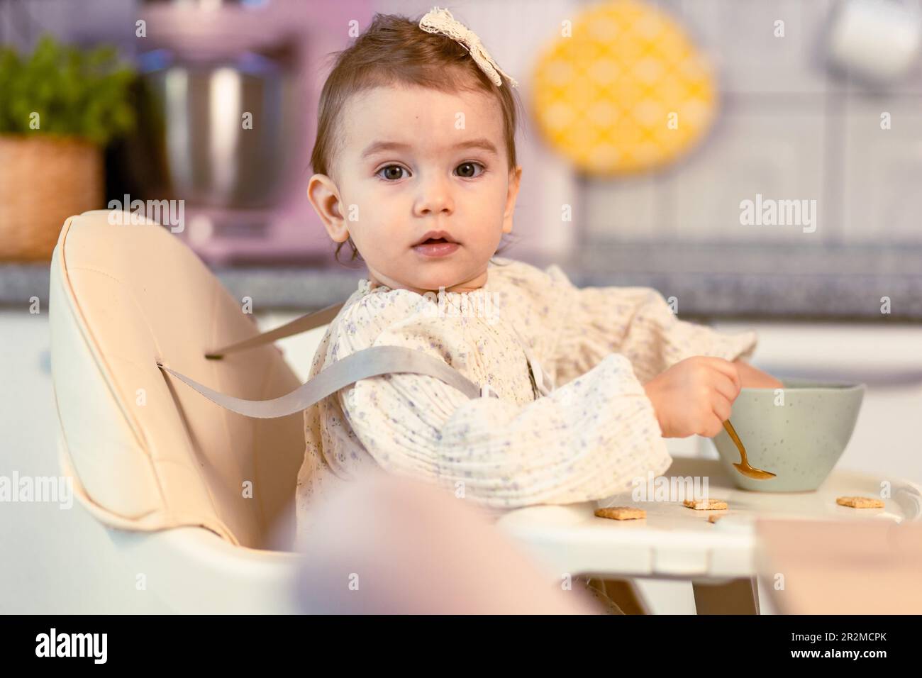 Little baby girl sitting in a highchair eating by herself with a spoon Stock Photo