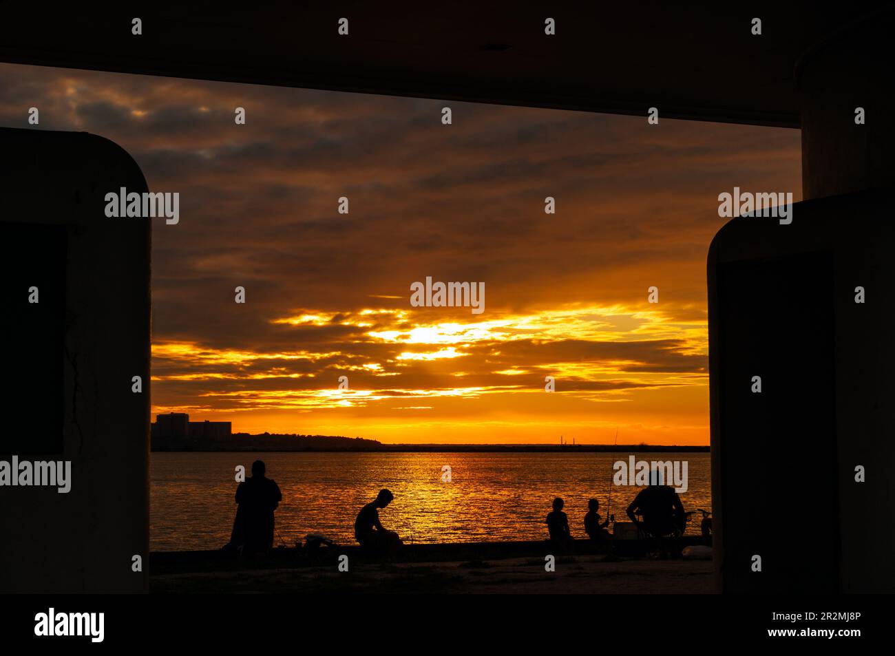 People fishing from a pier on the Lake Erie shore of Cleveland and silhouetted by the setting sun Stock Photo