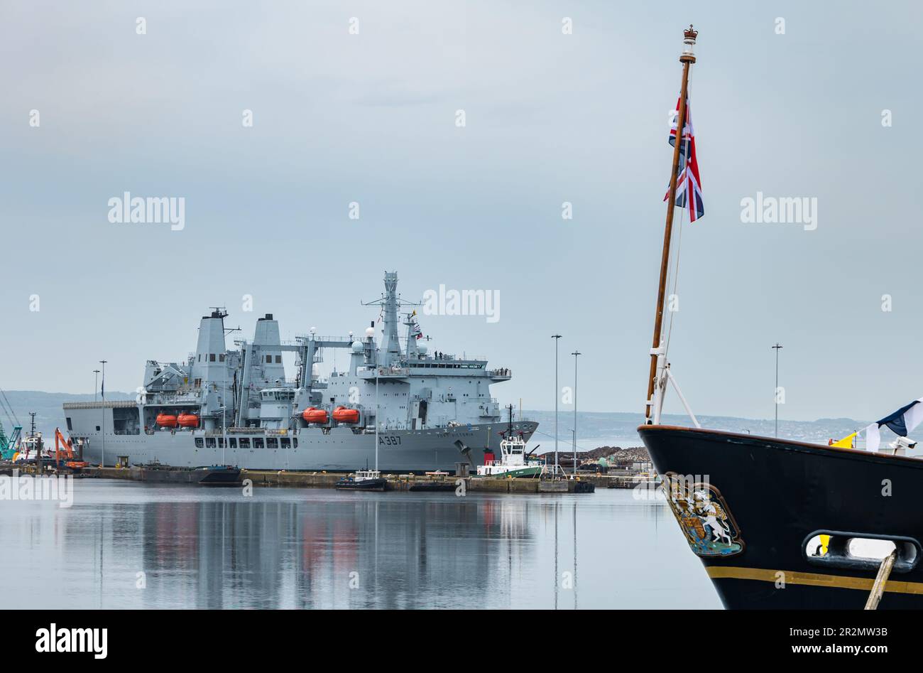 Edinburgh, Scotland, UK, 20th May 2023. RFA Fort Victoria (A387) enters Leith harbour: the combined fleet stores ship and tanker of the Royal Fleet Auxiliary of the United Kingdom tasked with providing ammunition, fuel, food and other supplies to British Royal Navy vessels is manoeuvred into the harbour to a mooring by tug boatspast the Royal Yacht Britannia. Credit: Sally Anderson/Alamy Live News Stock Photo