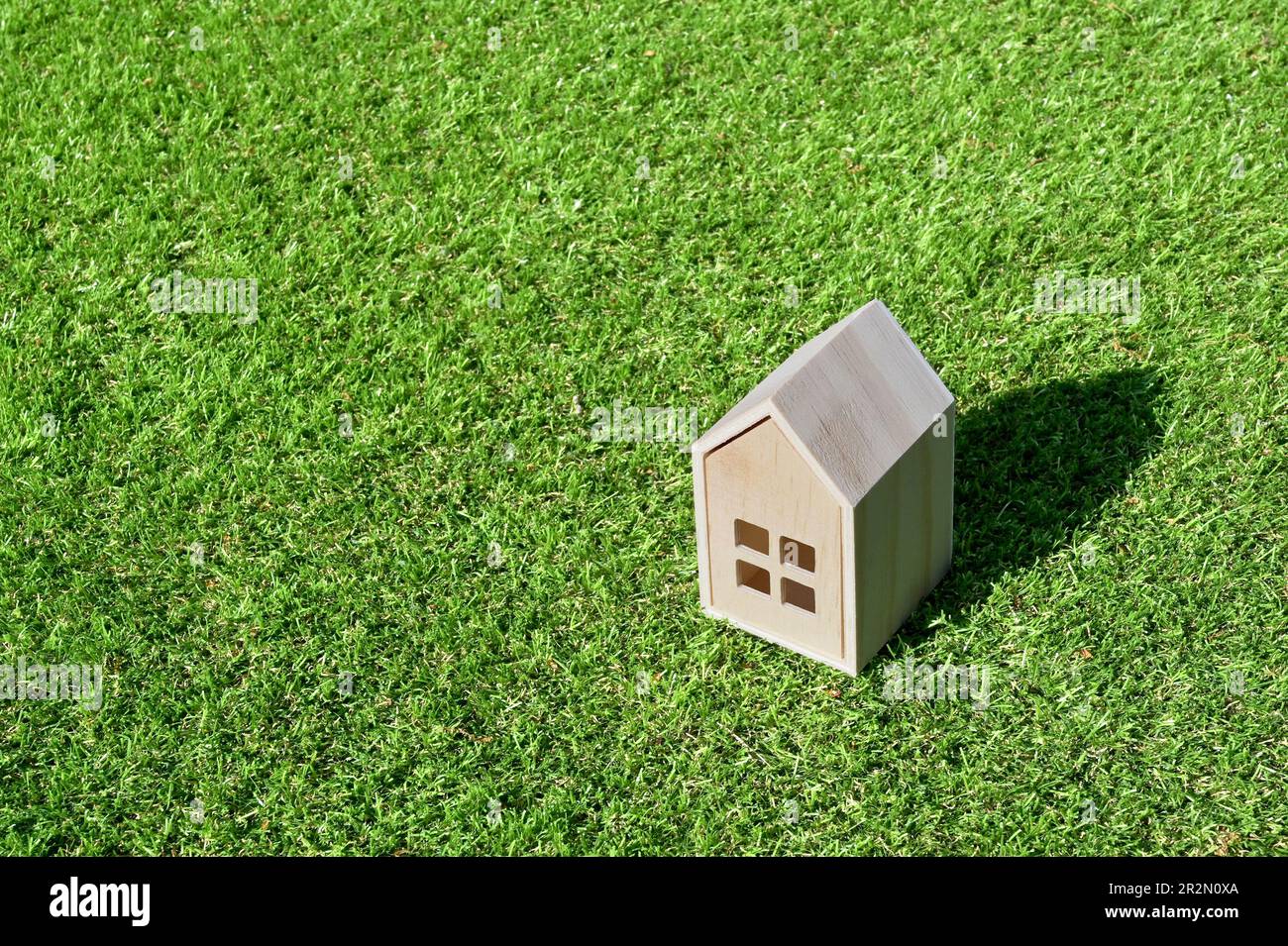 Small wooden model house on a background of short green grass. Housing concept. No people. Copy space. Stock Photo