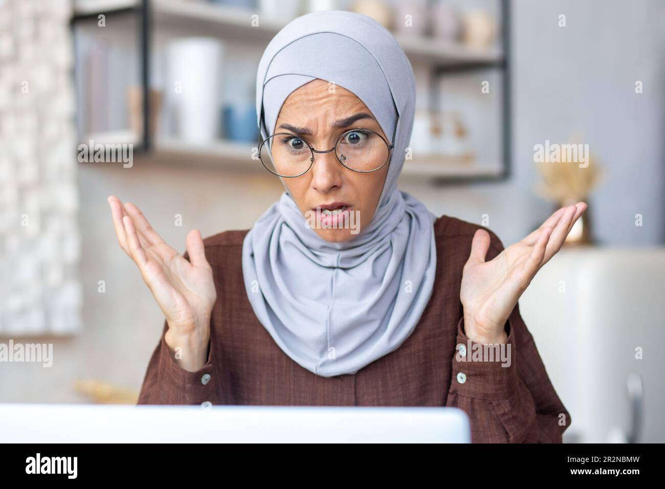 Close-up photo. A young Muslim woman in a hijab and glasses sits at ...