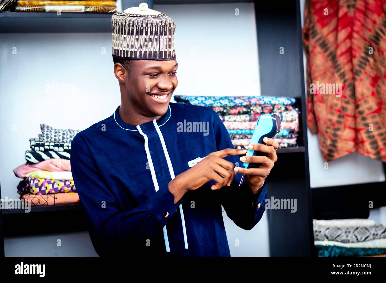 Photo of a black african man in a blue shirt typing code on a pos machine while standing Stock Photo