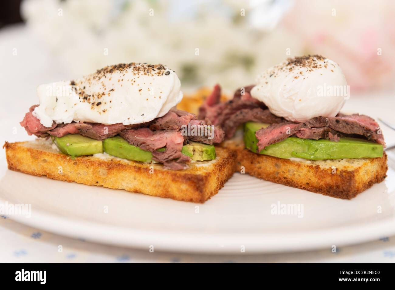 Steak benedict breakfast. Poached eggs, grilled steak and avocado on toast, with side of hash browned potatoes. Stock Photo