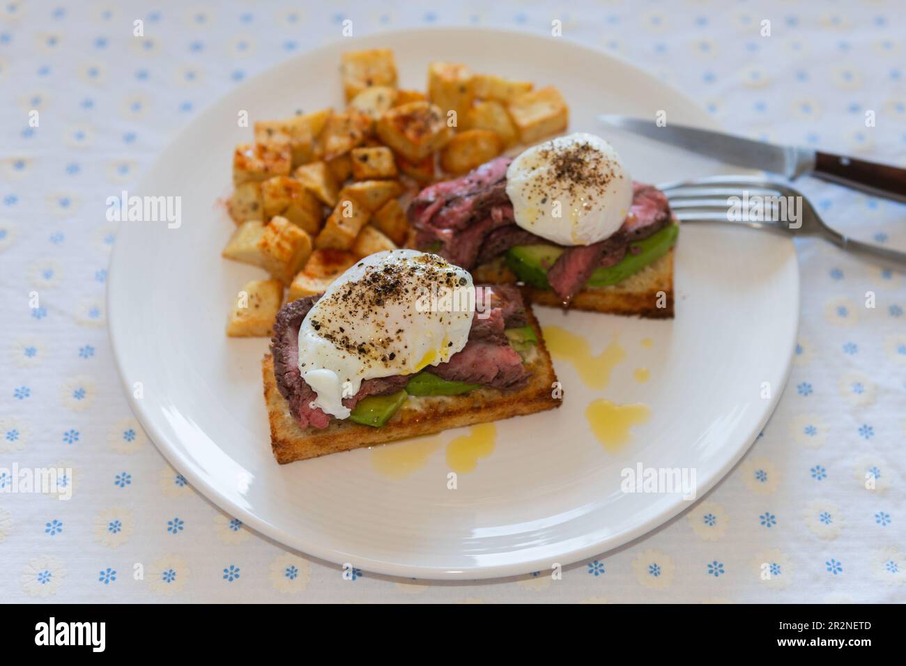 Steak benedict breakfast. Poached eggs, grilled steak and avocado on toast, with side of hash browned potatoes. Stock Photo