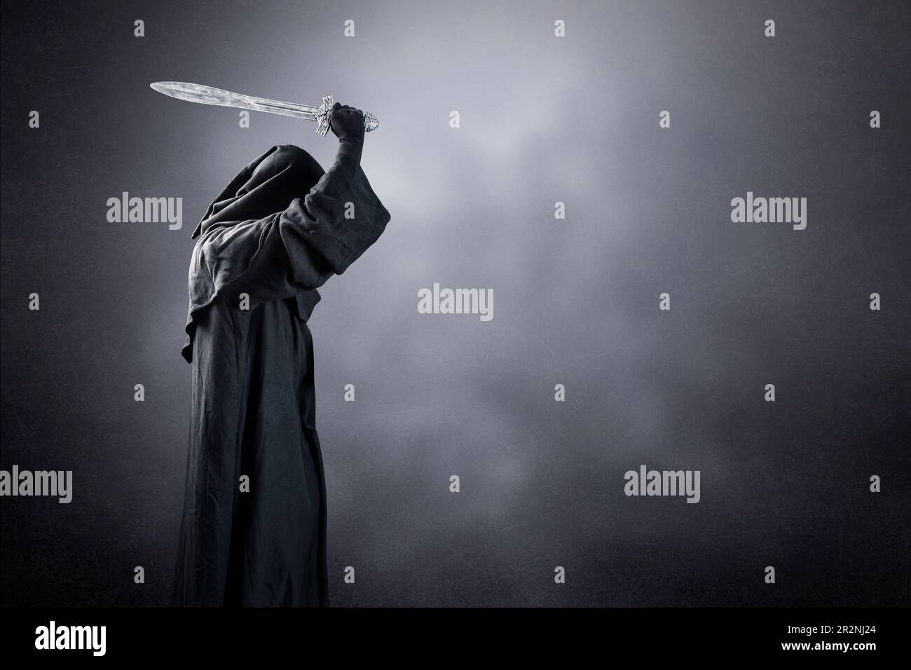 Dark knight with hooded cape and medieval sword over dark misty background Stock Photo