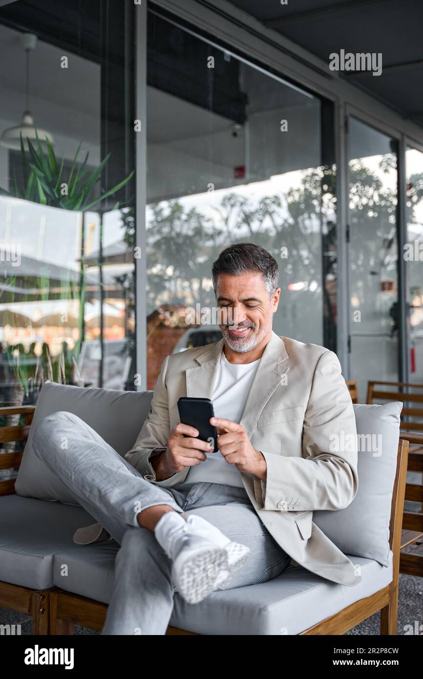 Happy relaxed mid aged business man sitting in outdoor cafe using smartphone. Stock Photo