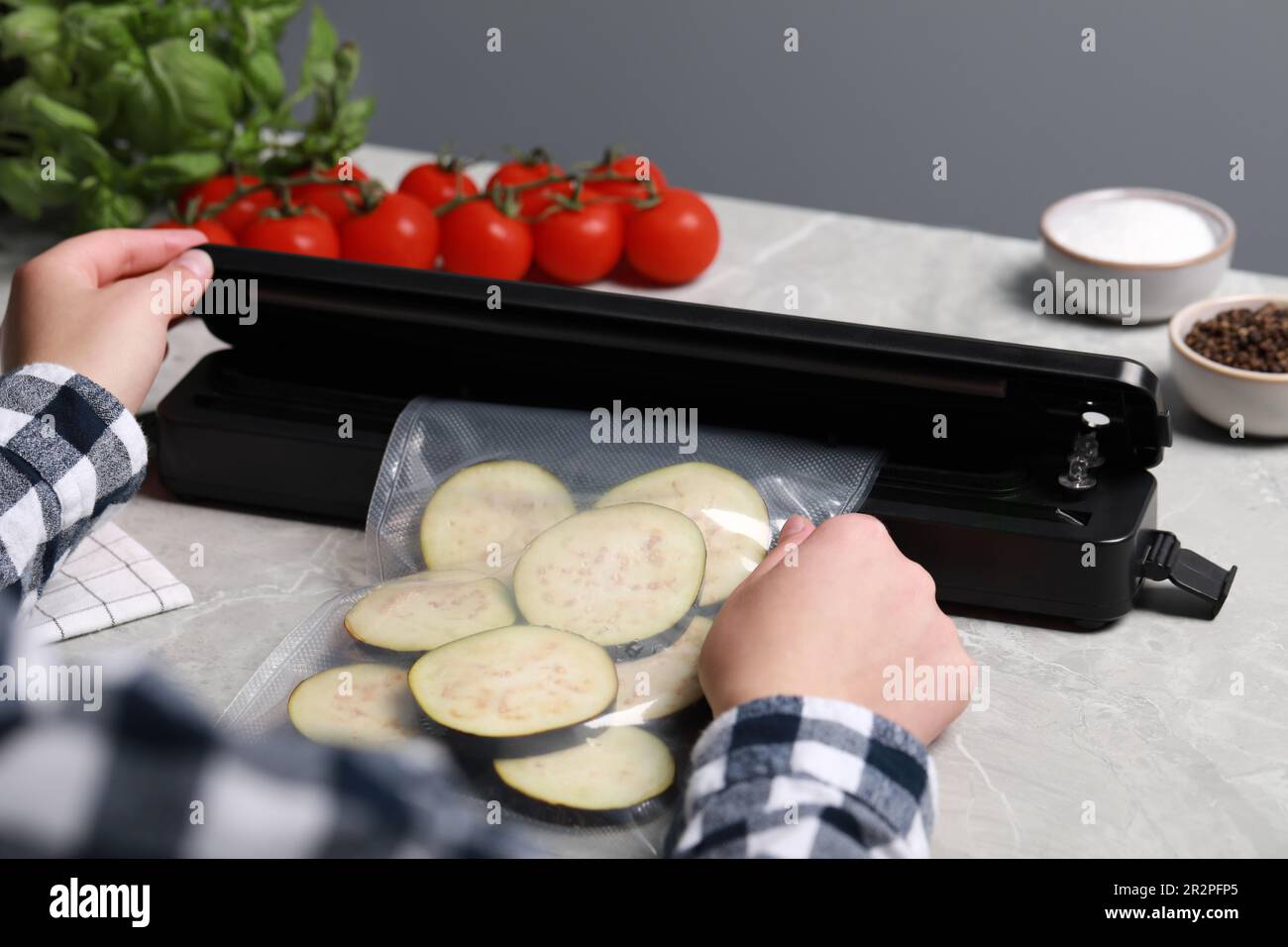 Woman packing cut eggplant into plastic bag using vacuum sealer on